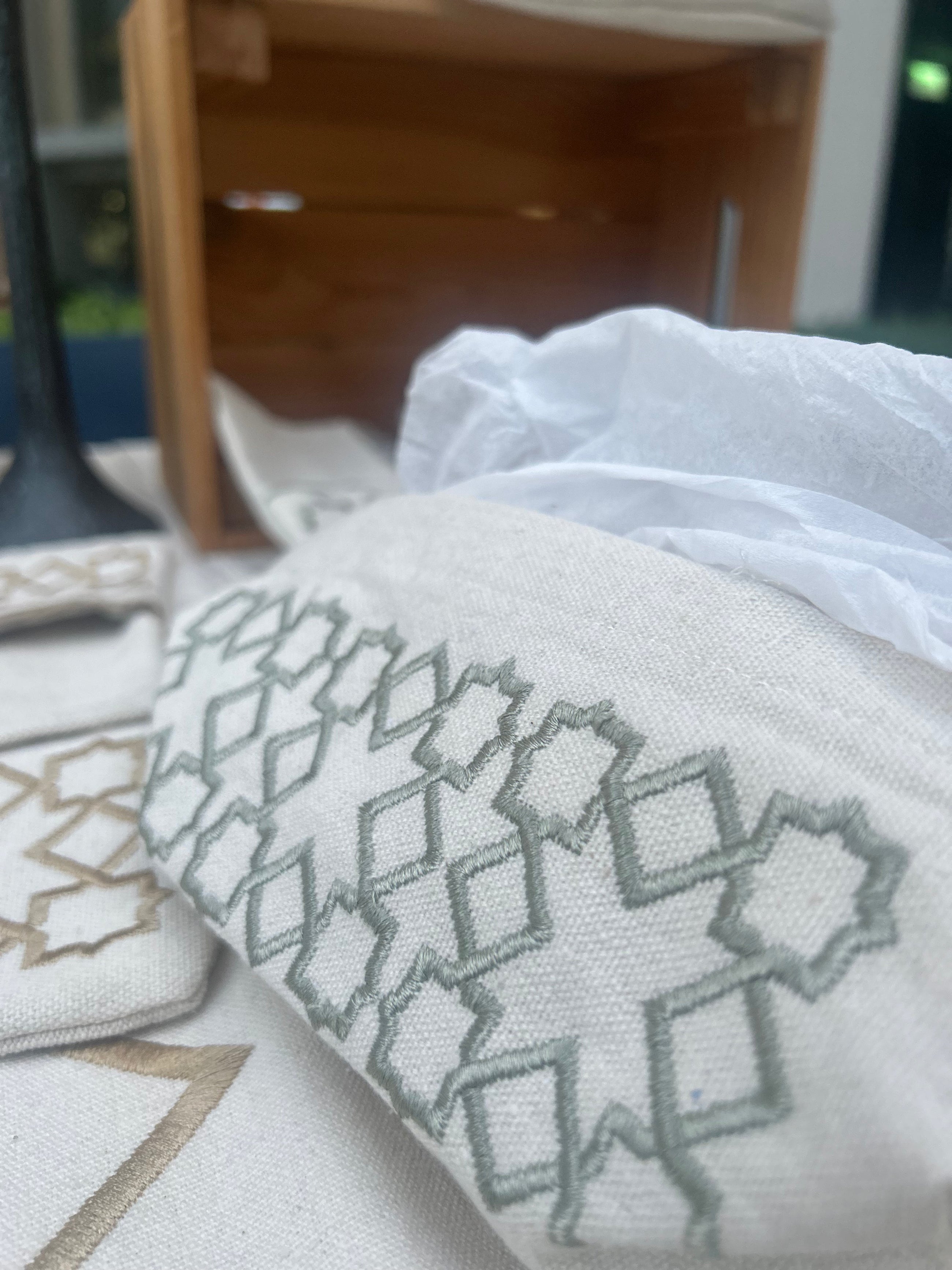 The Arabesque Table Set - 15 Piece Sage Embroidered set from Raw Cotton placed in a handmade basket with leather handles. This picture shows the tissue box cover.