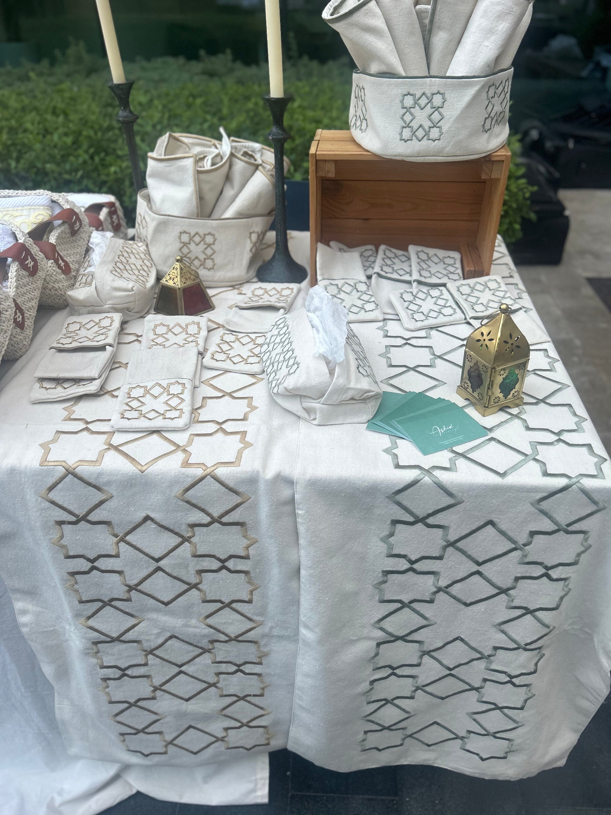 The Arabesque Table Set - 15 Piece Sage & Bronze Embroidered set from Raw Cotton placed in a handmade basket with leather handles.