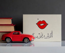 Greeting card featuring a contemporary Arabic love phrase "A Thousand Kisses" in a colourful graphic composition
