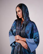 Upper-body view showing the blue patterned fabric, headscarf and pale blue cuffs.