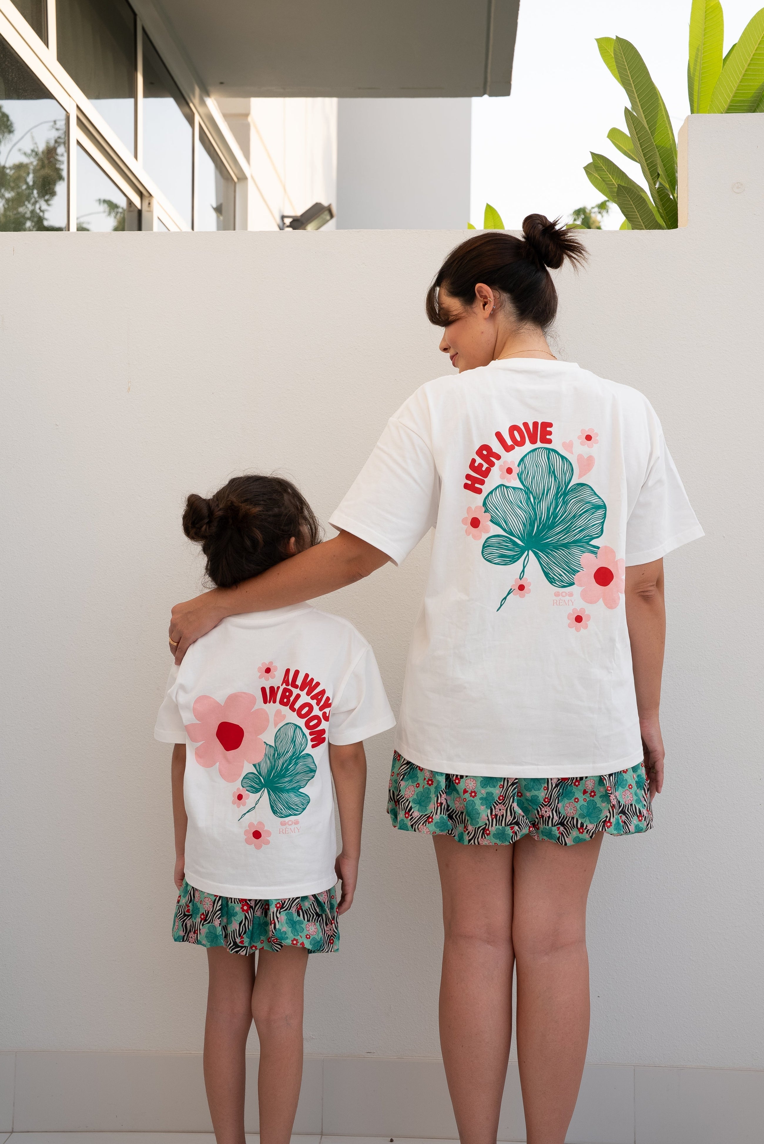 Woman and child wearing the EOS x Rémy Bloom oversized white cotton T-shirt, back view featuring the floral graphic print.