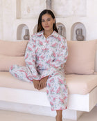 Layla Pink Long PJ Set – model seated on sofa with hands resting in lap, wearing white long-sleeve pyjama set with pink cheetah print and pink piping detail