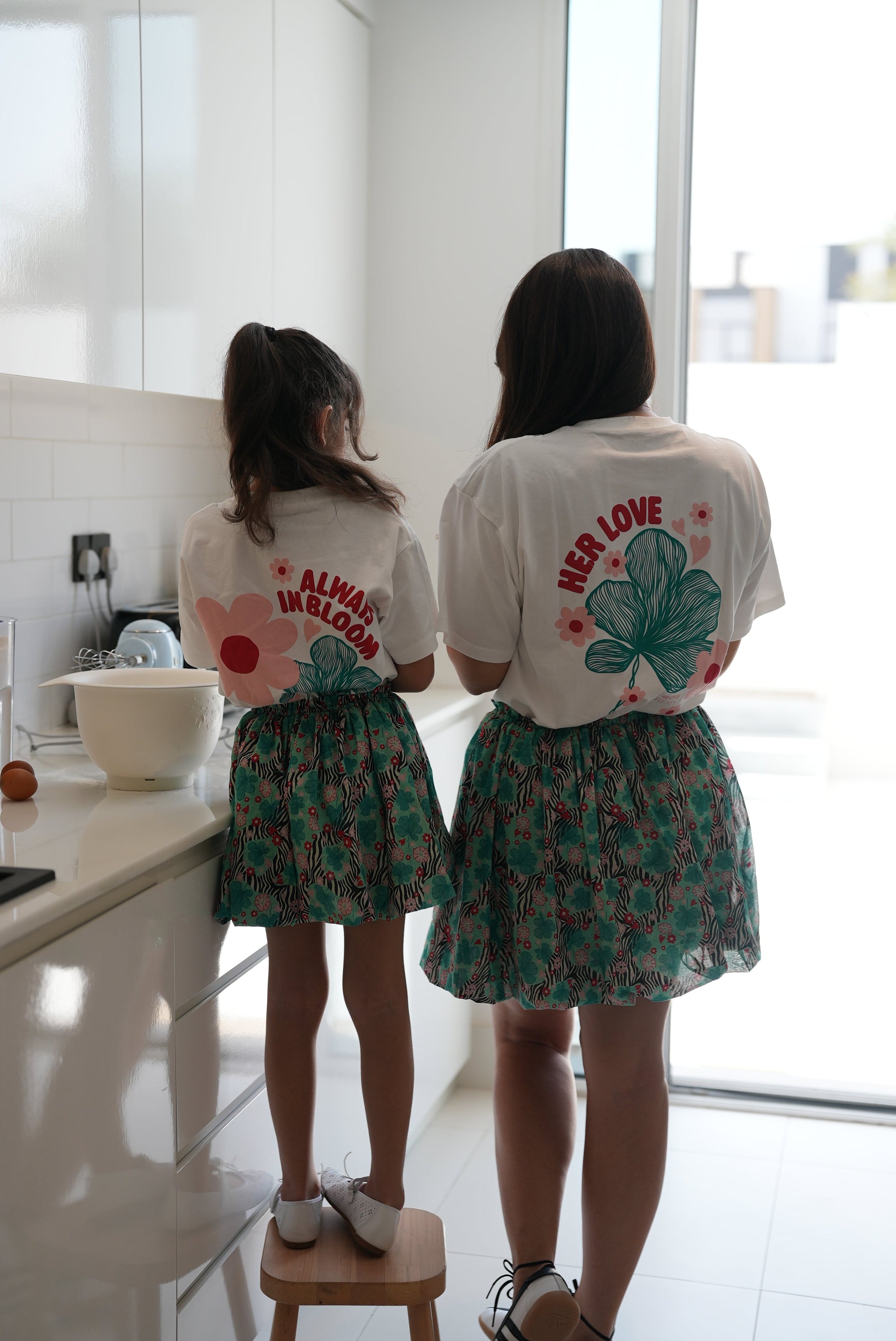 Woman and child wearing the EOS x Remy Bloom oversized white cotton T-shirt, back view with floral graphic artwork.
