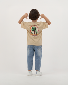 Kid boy in beige The Palm T-Shirt featuring colorful palm trees.