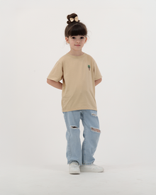 Child girl wearing The Palm beige T-Shirt with tropical leaf print.