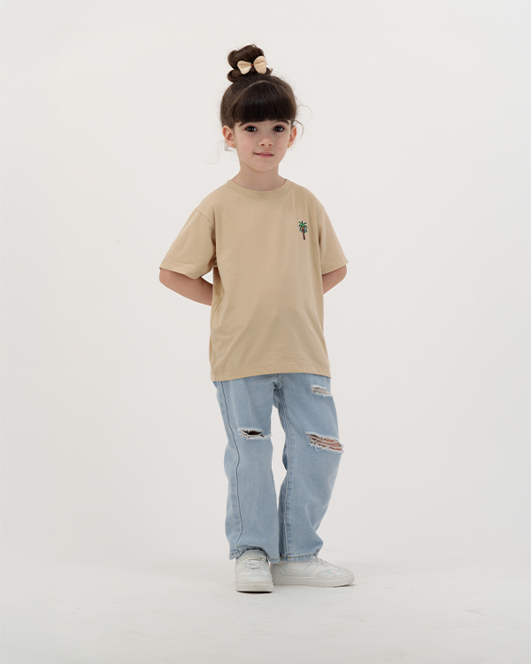 Child girl wearing The Palm beige T-Shirt with tropical leaf print.