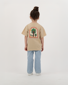 Girl modeling The Palm Kids beige T-Shirt featuring colorful palm print.