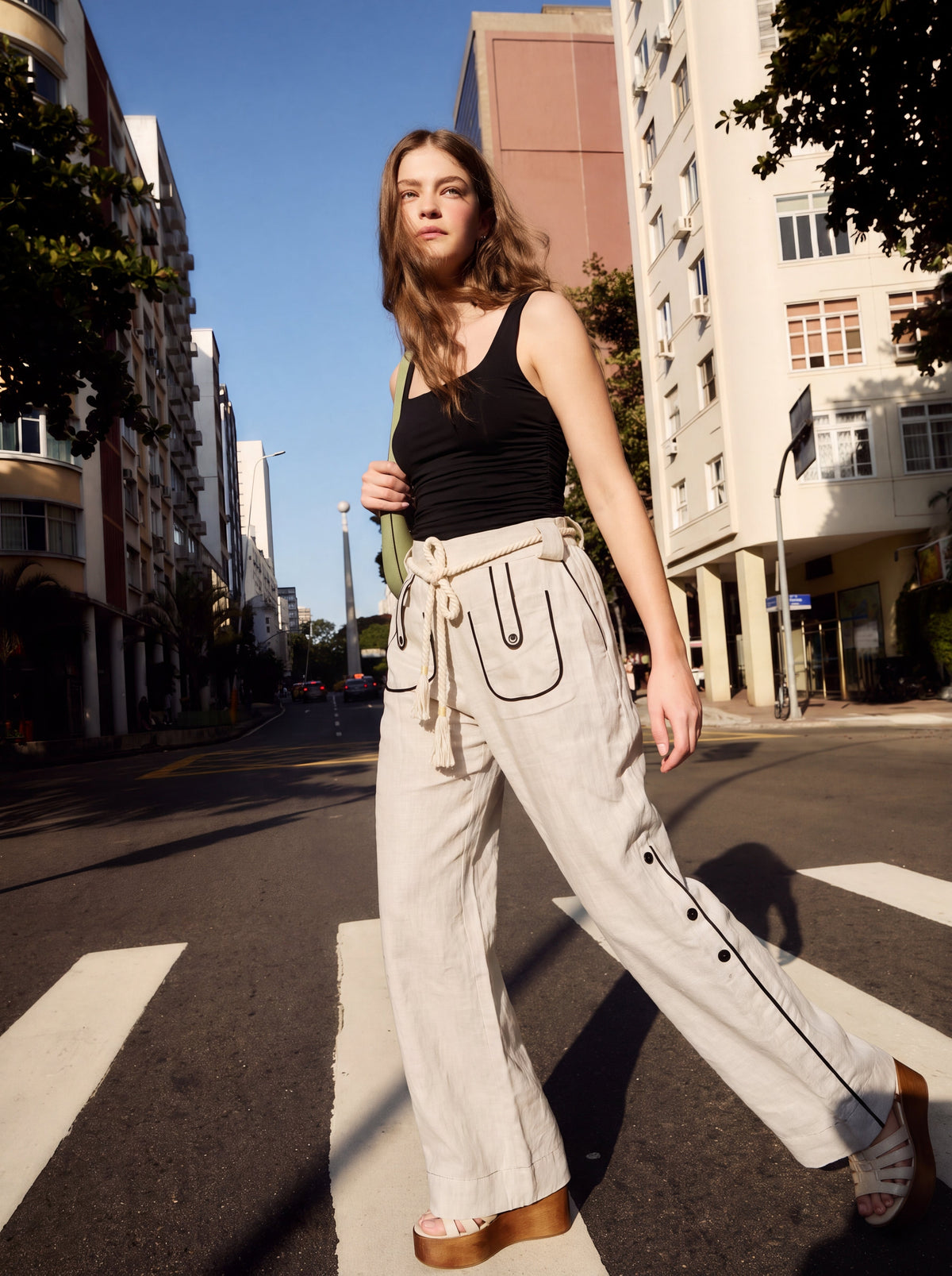 Model crossing the street, wearing the Aether Linen Trouser in beige by Muda Clothing 