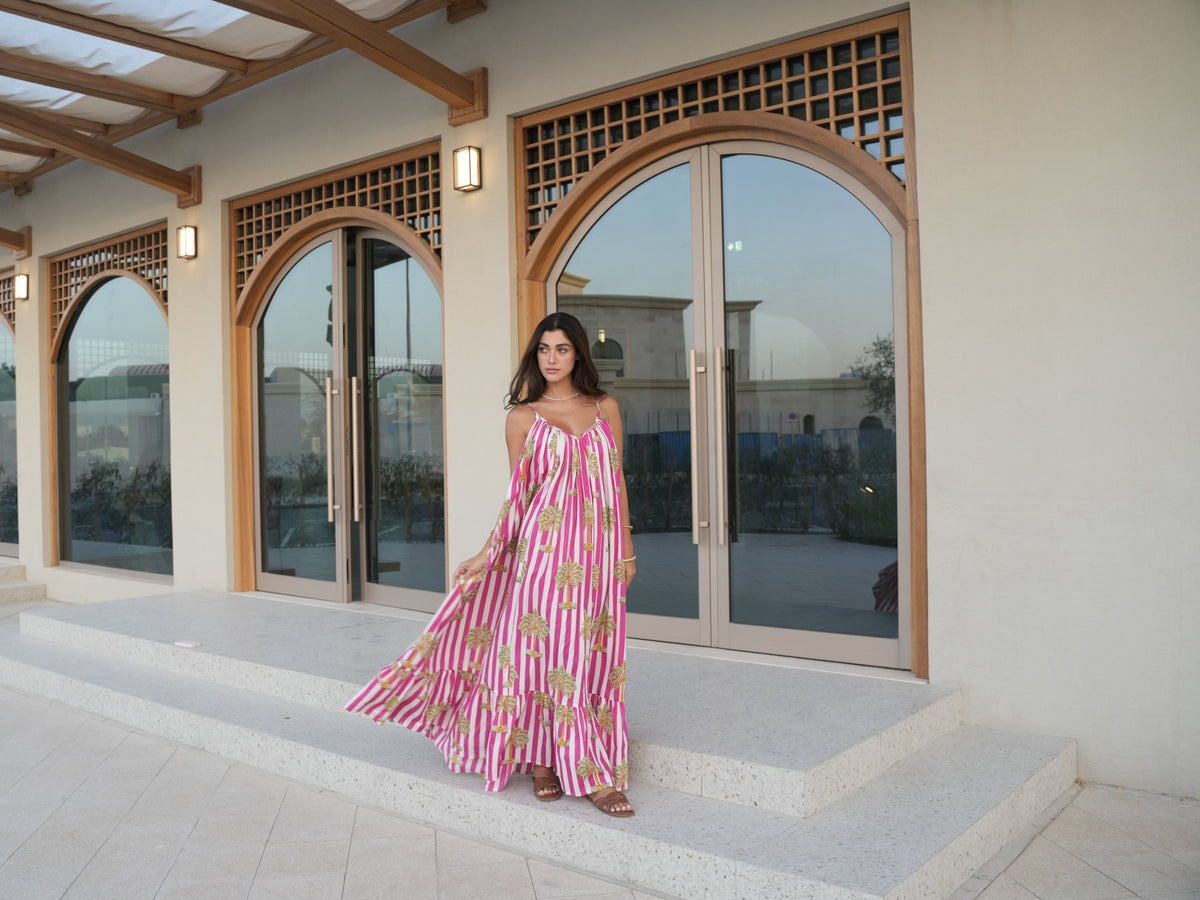 A model in a pink and white palm-print maxi dress by Kyshmysh, mid-twirl beneath arched doors at golden hour
