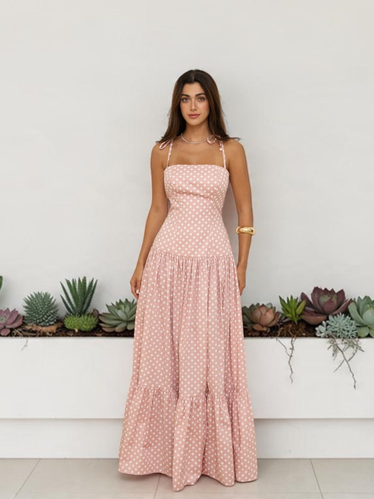 Model in a pink polka-dot maxi dress by Hazar Azhari, standing in front of a white planter of succulents